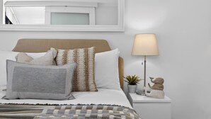 Une chambre à coucher bien rangée, avec un lit, une lampe de chevet et une table de chevet agrémentée d’une plante et d’un objet décoratif.