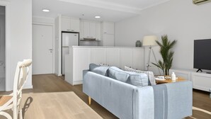 Un salon moderne avec un canapé, un téléviseur et une cuisine en arrière-plan.