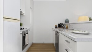 Une cuisine compacte avec des meubles blancs, un four encastré et un plan de travail doté d’un évier et d’objets décoratifs.