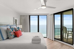 Ein Schlafzimmer mit einem großen Bett, einem Deckenventilator, Meerblick und einem Balkon mit einem Stuhl.