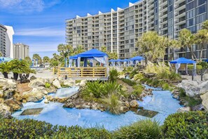 Ein Resort mit Poolbereich, einer Holzterrasse und einem großen Gebäude im Hintergrund.
