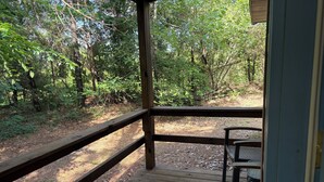 A wooden deck with a metal bench, surrounded by dense forest. - Shawnee Pines #3 - Cozy Cabin (Golconda)