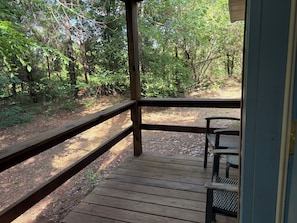 A wooden deck with a metal bench, surrounded by dense forest.