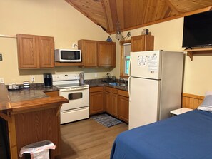 A compact kitchen with wooden cabinets, a microwave, stove, refrigerator, and a small sink.