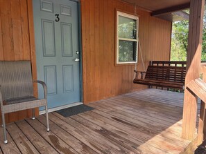 A wooden porch with a blue door, a wicker chair, and a wooden bench.