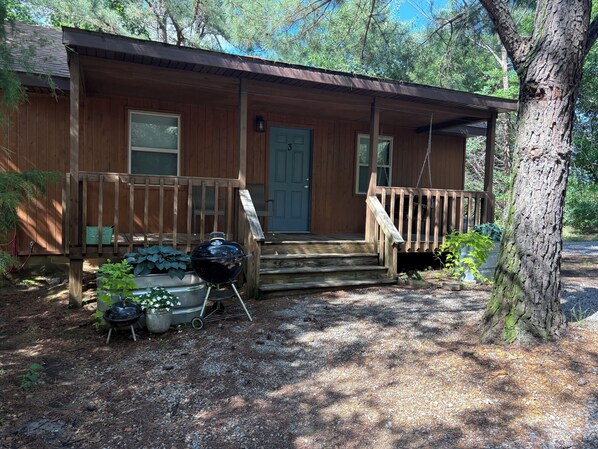 A wooden cabin with a porch, a door, and a grill outside.