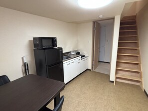 A compact kitchen with a refrigerator, microwave, and sink. There is a dining table with chairs and a staircase leading to another room. - Dashing House Momoya 2 (大阪市)
