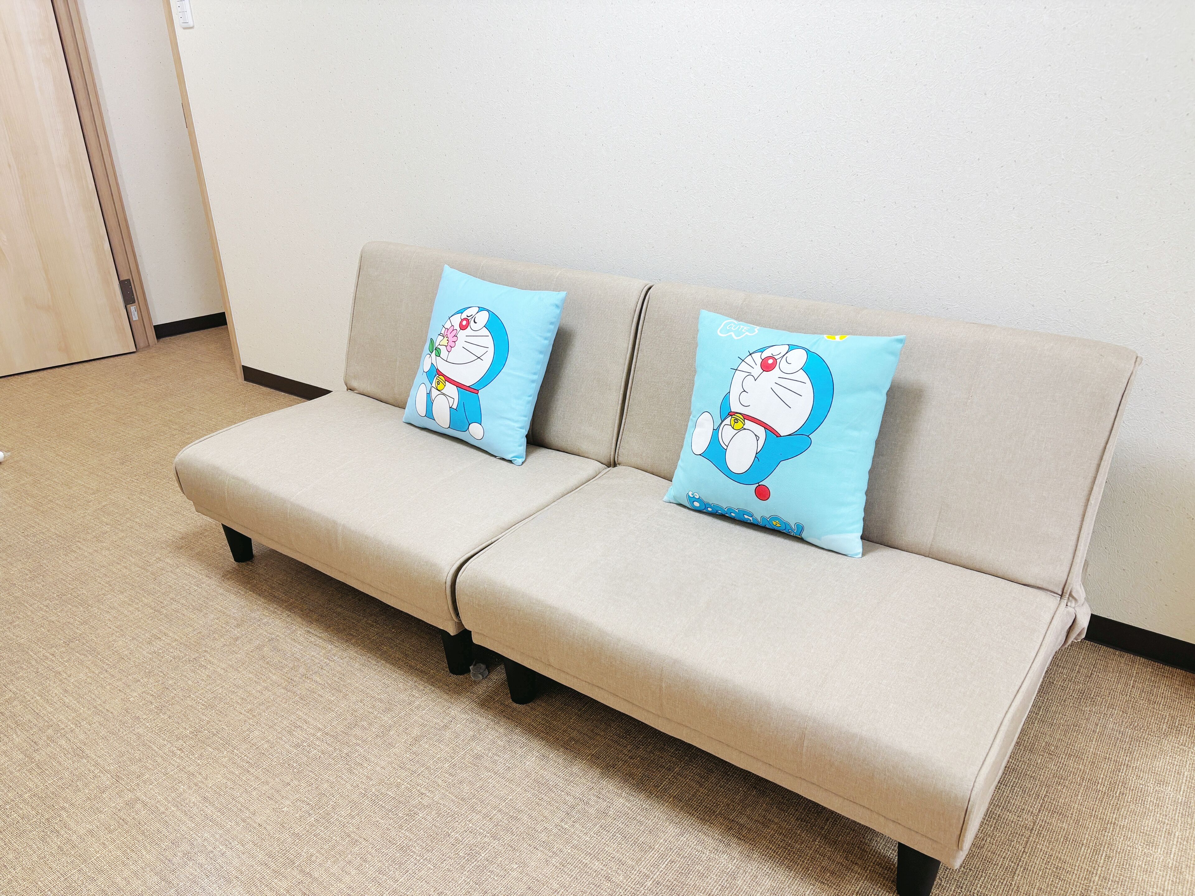 Ein beiges Sofa mit zwei hellblauen Kissen, verziert mit einer Zeichentrickfigur.