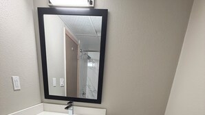 Et badeværelse med en hvid vask, toilet, spejl og en hylde med sammenfoldede håndklæder.