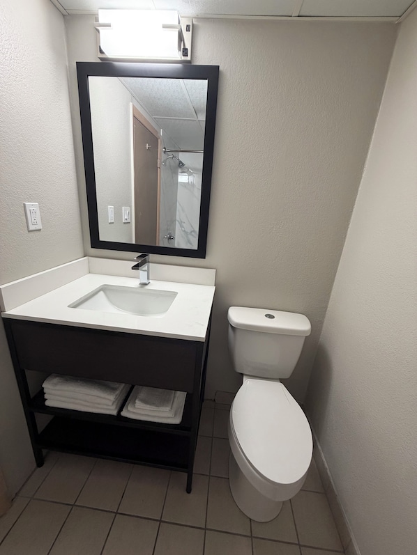 A bathroom with a white sink, a toilet, a mirror, and a shelf with folded towels.