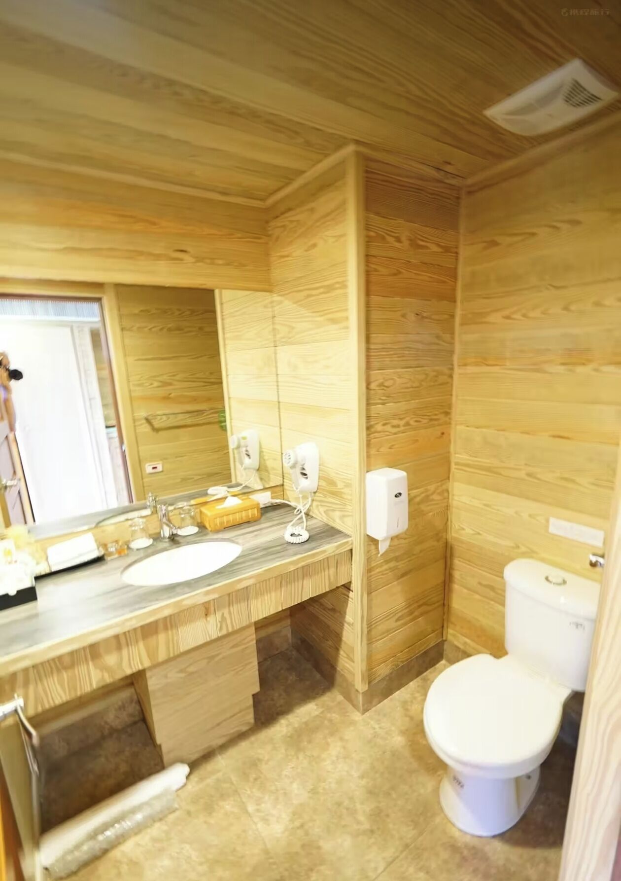 Une salle de bain avec un mur en bois, un lavabo, un miroir, des toilettes et un porte-serviettes.