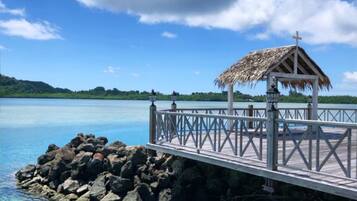 A pier with a thatched-roof structure, a railing, and a view of calm water and greenery.