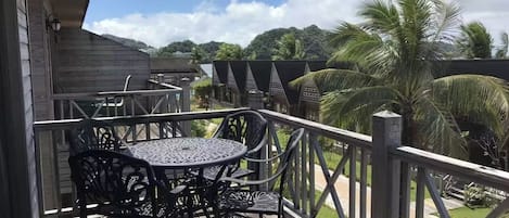 Une terrasse en bois, agrémentée d’une table et de chaises en métal, entourée d’une rambarde, et offrant une vue sur un paysage de palmiers et le ciel.