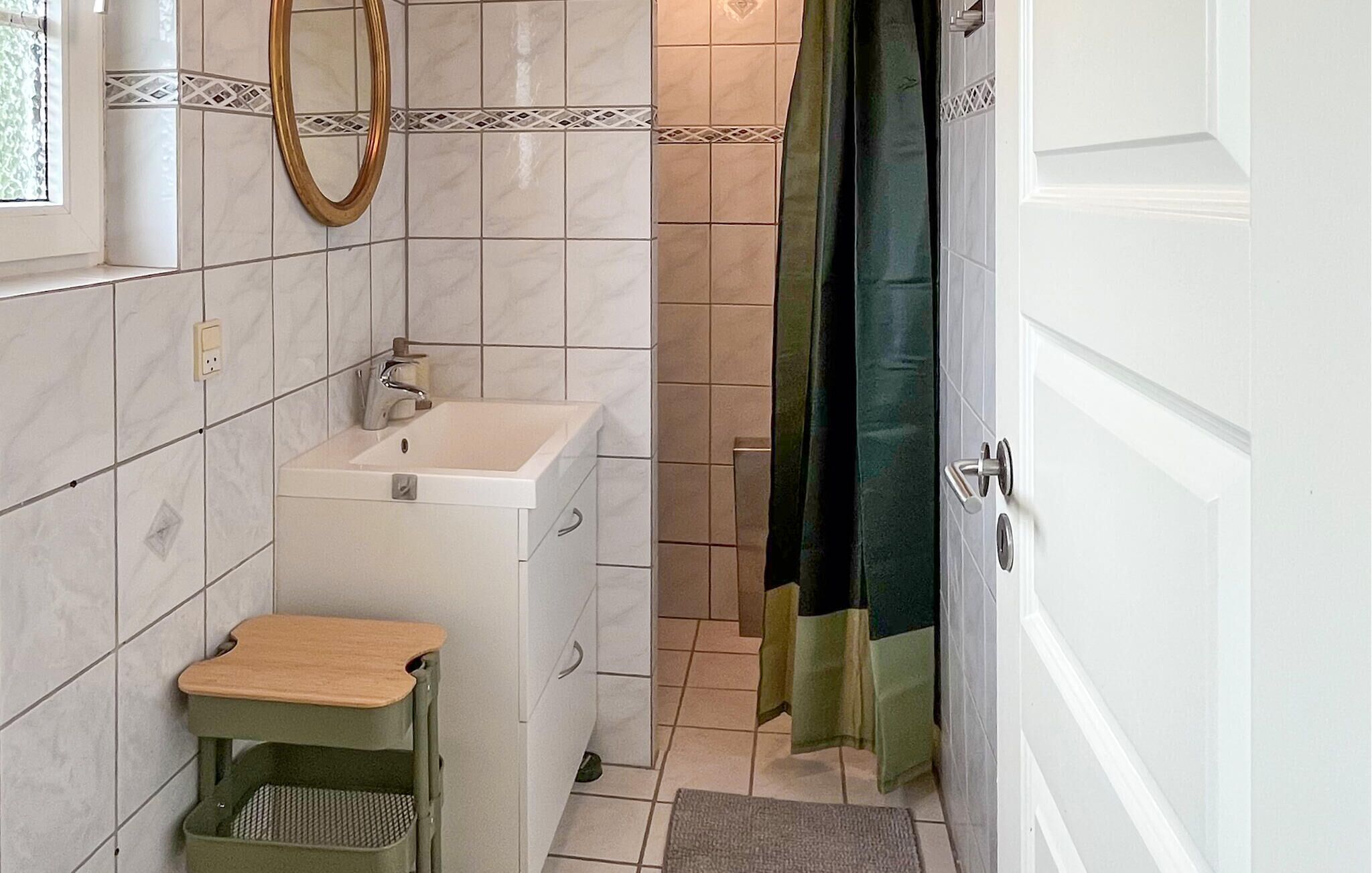 Ein Badezimmer mit Waschbecken, Spiegel, Handtuchhalter, Duschvorhang und einem kleinen Hocker.