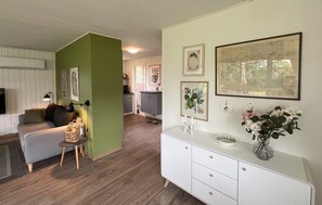 A living room with a green accent wall, a white sofa, a small side table, and a white cabinet with decorative items. - 2 bedroom stunning home in Broager (Broager)