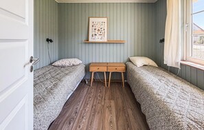 A room with two single beds, a wooden nightstand with drawers, a framed botanical print on the wall, and a window with curtains. - 2 bedroom stunning home in Broager (Broager)