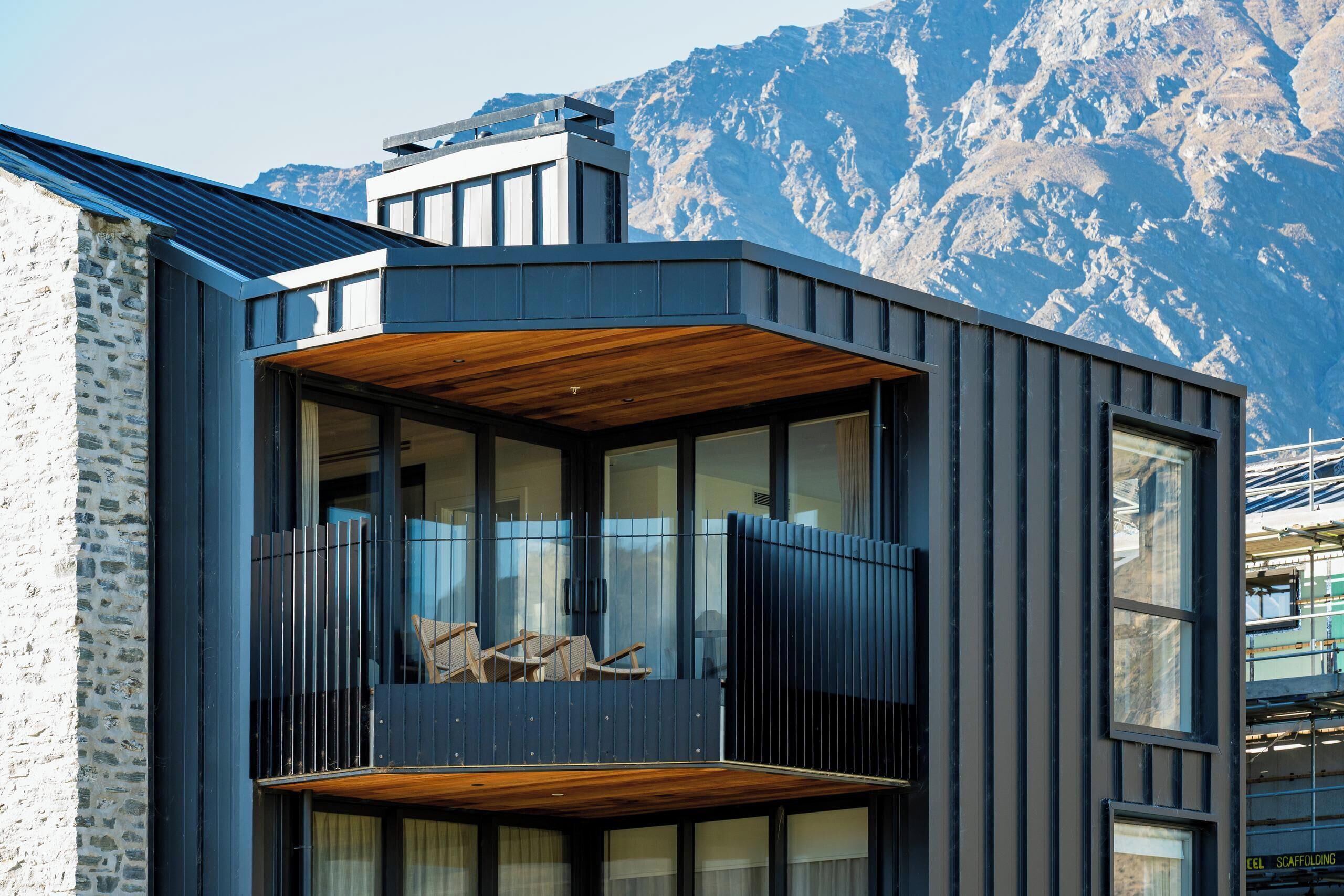 A modern building with a balcony, large windows, and a mountainous backdrop.