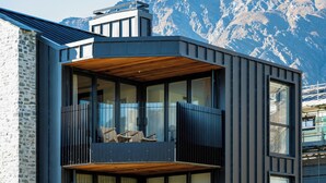 Een modern gebouw met balkon, grote ramen en een bergachtige achtergrond.