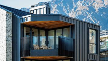 A modern building with a balcony, large windows, and a mountainous backdrop.