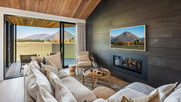 Een moderne woonkamer met een grote bank, een ronde salontafel met een schaal lekkernijen, een open haard en een groot raam met uitzicht op de bergen.