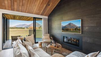 A modern living room with a large sofa, a round coffee table with a tray of snacks, a fireplace, and a large window with a mountain view.