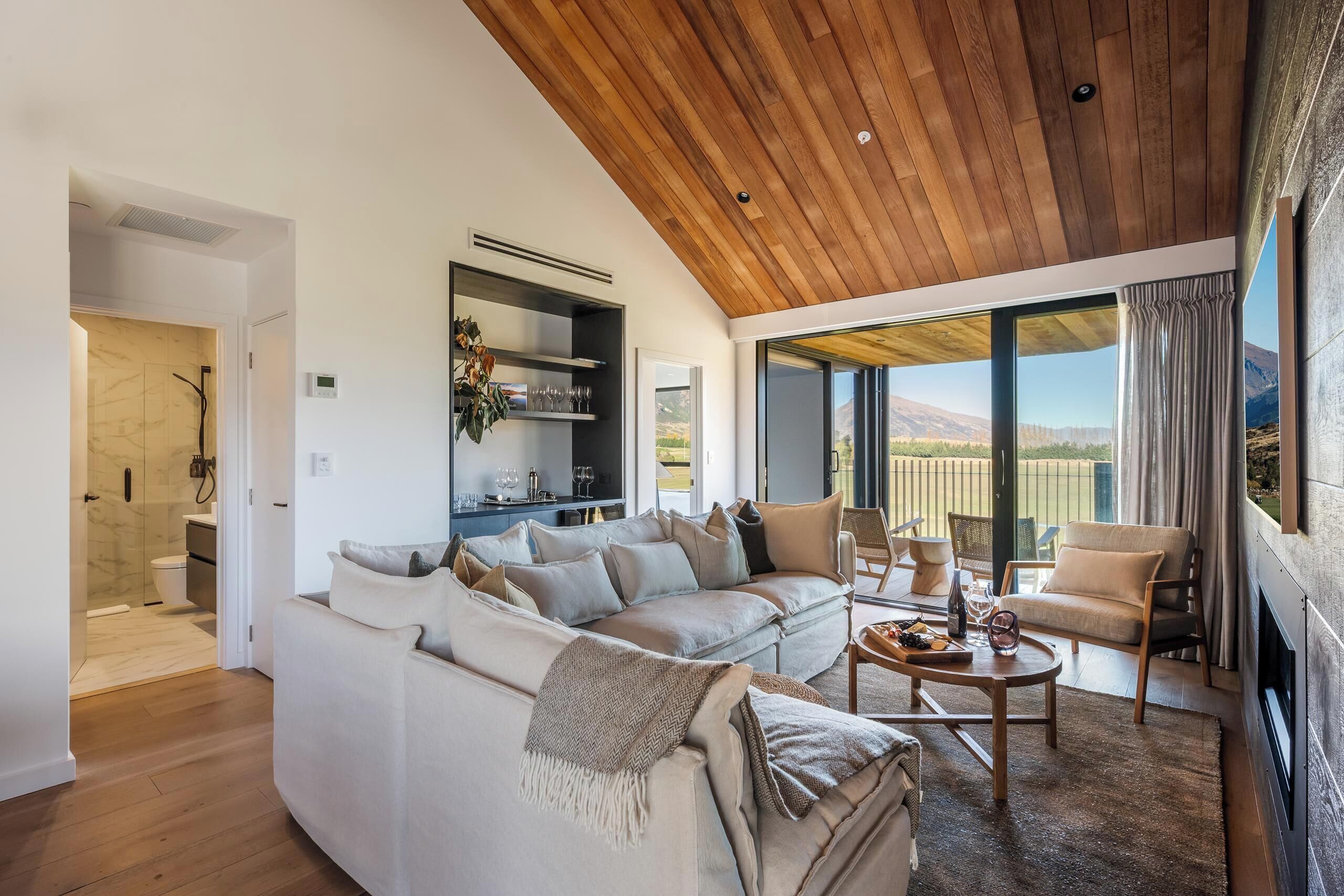 A modern living room with a wooden ceiling, a white sofa, a coffee table, and a view of the outdoors.
