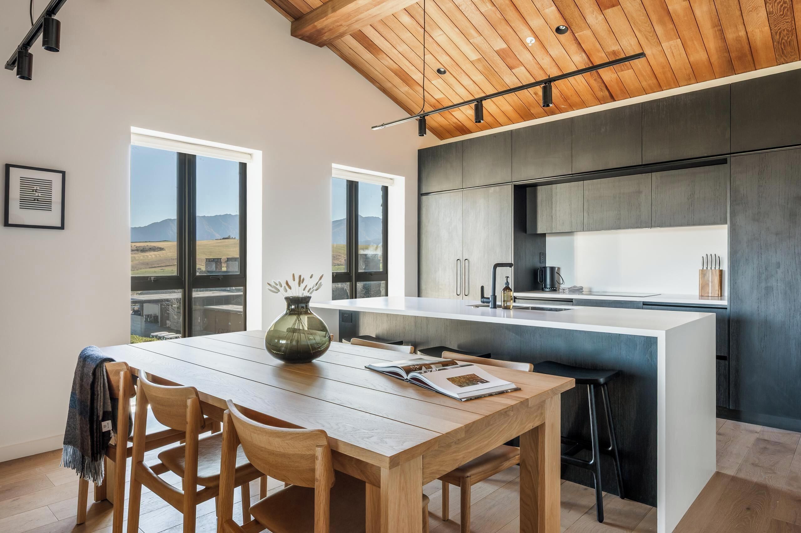 A modern kitchen with a central island, wooden dining table, and chairs.