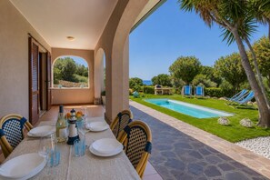 Un espace extérieur abrité, aménagé pour les repas, avec une piscine et des chaises longues en arrière-plan.