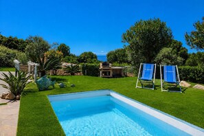 Ein Schwimmbecken mit freiem Blick auf das Meer, ein Grillbereich und zwei blaue Liegestühle.
