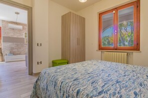 Ein Schlafzimmer mit Bett, Kleiderschrank, Heizkörper und einem Fenster mit Blick auf Bäume.