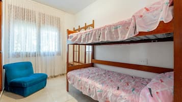 Une chambre avec un lit superposé, une chaise bleue et une fenêtre ornée de rideaux légers.