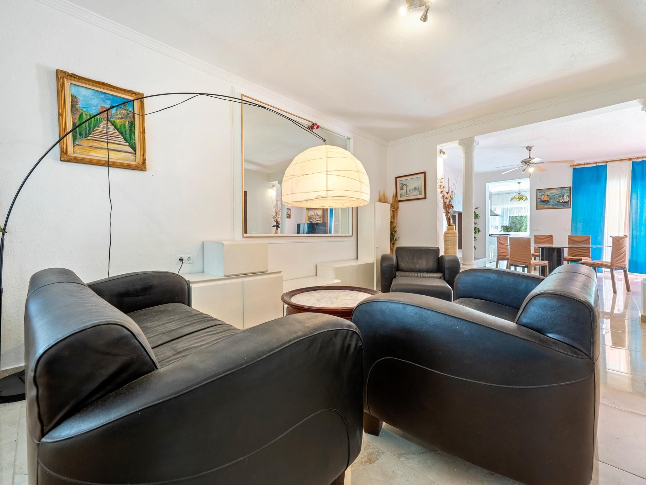 Uma sala de estar moderna com um sofá, uma área de jantar com cadeiras, um espelho grande e uma luminária pendente.