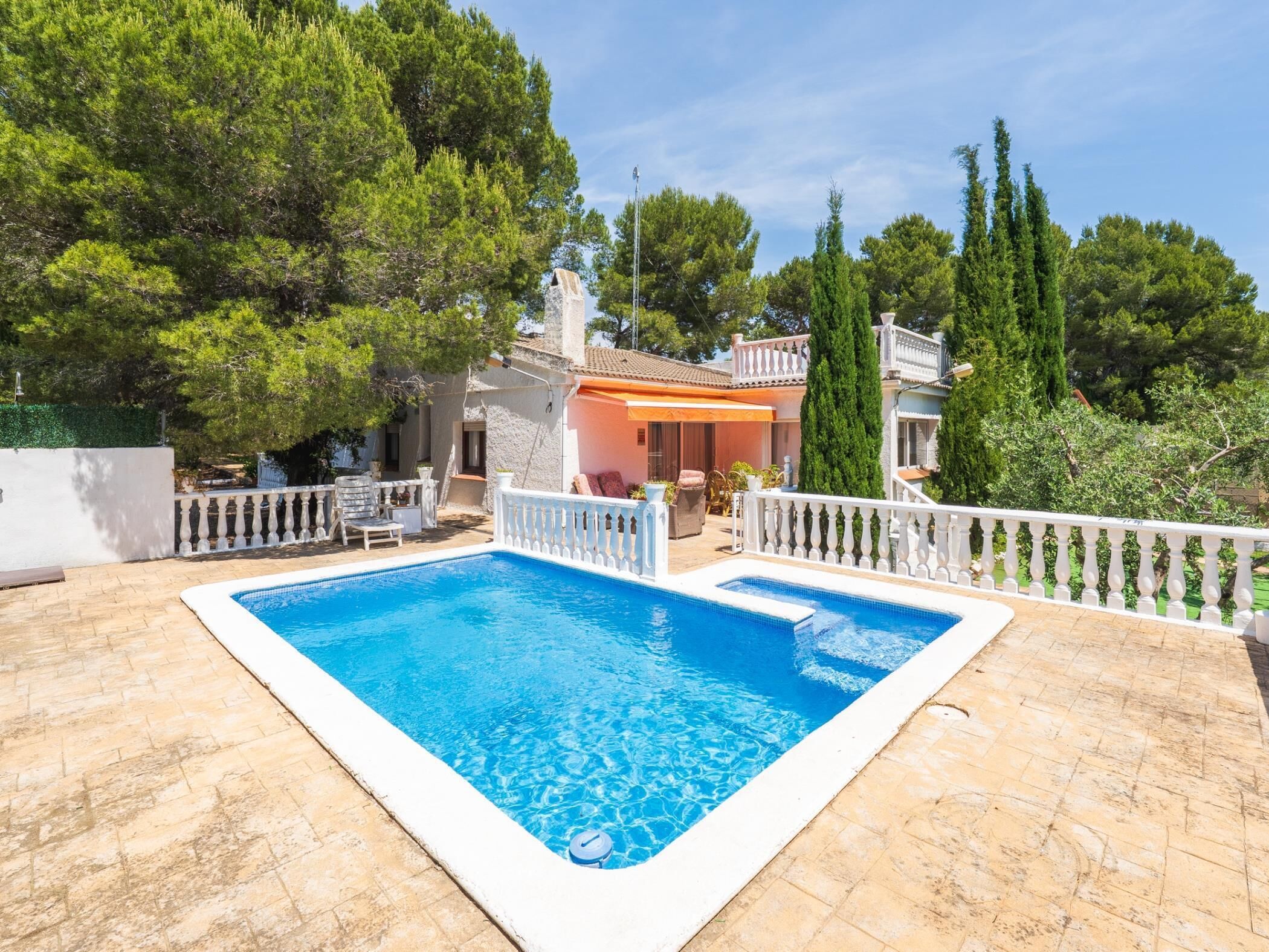 A rectangular swimming pool with a white deck edge, surrounded by a white balustrade.