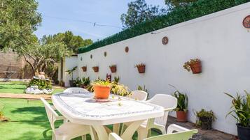 Eine Terrasse mit Tisch und Stühlen, umgeben von Kübelpflanzen und einer weißen Wand mit dekorativen Tellern.