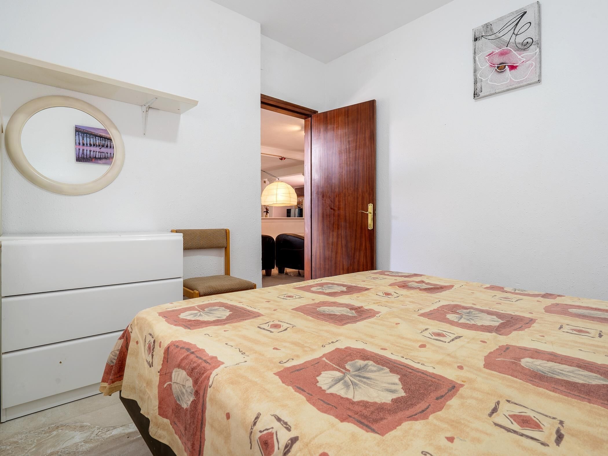 A bedroom with a bed, a dresser, a chair, a wooden door, and a wall-mounted picture.
