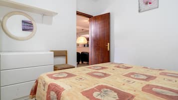 A bedroom with a bed, a dresser, a chair, a wooden door, and a wall-mounted picture.