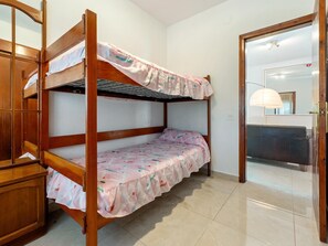 Uma cama de solteiro com colcha estampada, um guarda-roupa de madeira e uma porta que dá para o banheiro.