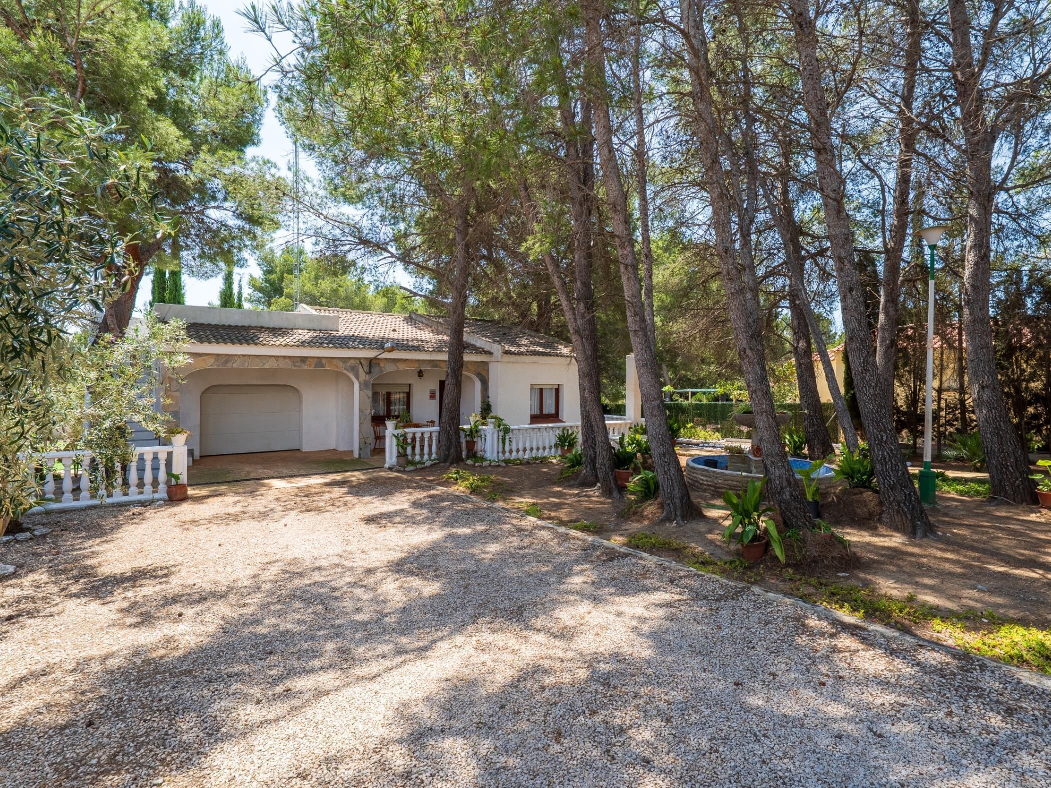 A house with a covered porch, a garage, and a gravel driveway surrounded by trees.