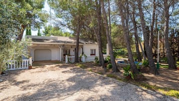 A house with a covered porch, a garage, and a gravel driveway surrounded by trees.
