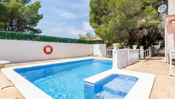 Ein rechteckiger Swimmingpool mit weißem Rand, eine weiße Wand mit einem roten Rettungsring und ein weißer Zaun mit Blumentöpfen.