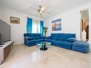 A living room with a sectional sofa, a glass coffee table, a ceiling fan, and a painting of a bridge. - Private pool house, barbecue and petanque (L'Ametlla de Mar)