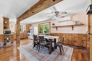 A kitchen with wooden cabinets, a dining table with chairs, a ceiling fan, and a window with a view of greenery. - Walnut Grove- fenced yard- rural getaway (Coloma)