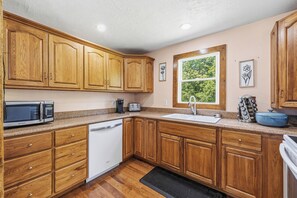Una cocina con armarios de madera, microondas, tostadora, fregadero y ventana con vistas a la vegetación.
