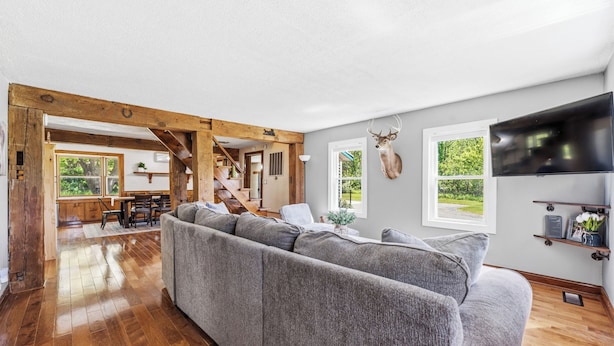 Ein geräumiges Wohnzimmer mit einer großen, grauen Eckcouch, Holzbalken, einem aufgehängten Hirschgeweih und einem Fernseher an der Wand.