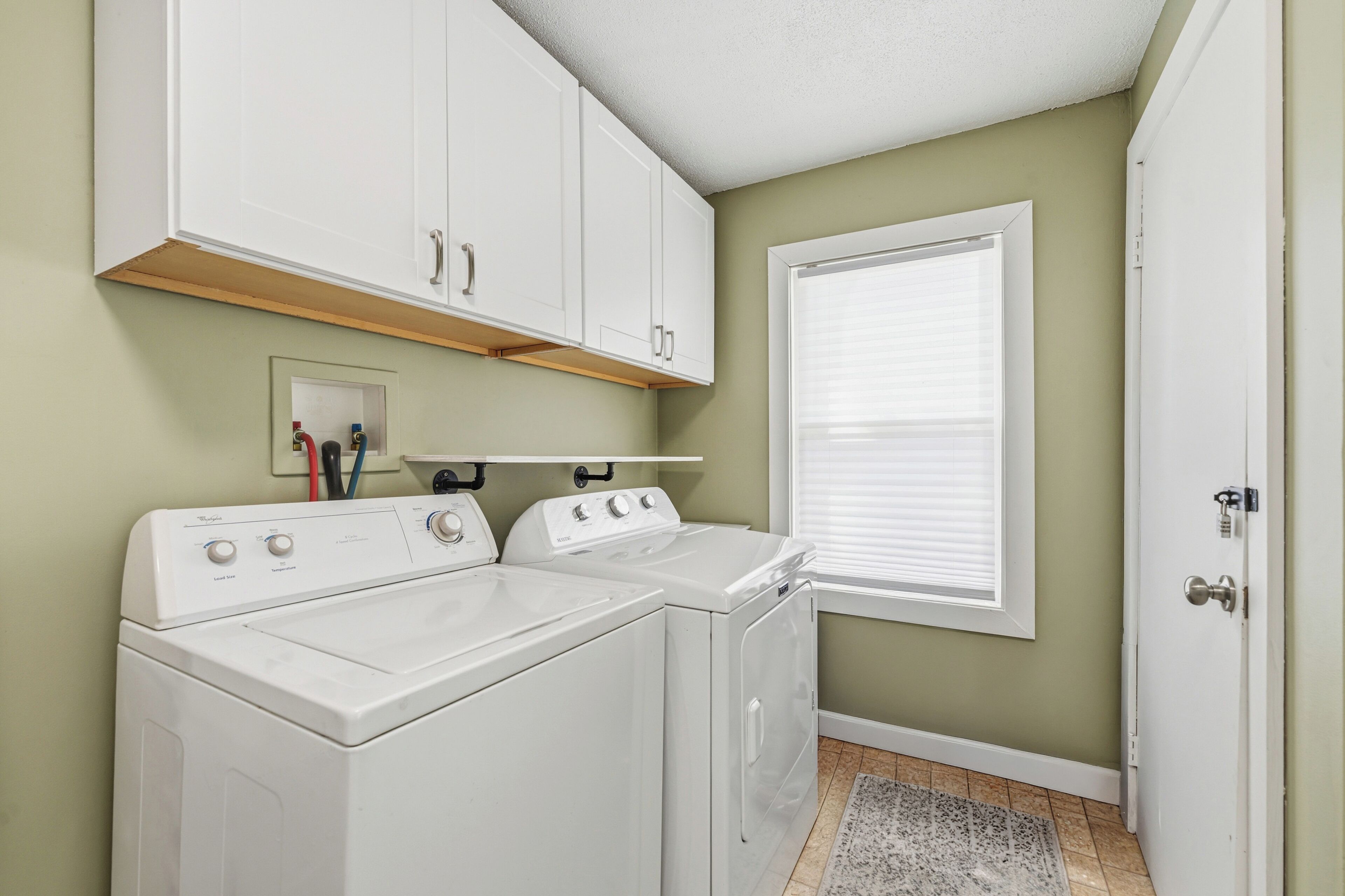 A laundry room with a washer and dryer, a shelf with toiletries, and a window with blinds.