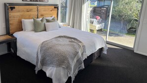Une chambre à coucher avec un grand lit, une tête de lit en bois, une vue sur l’extérieur et un tableau encadré au mur.