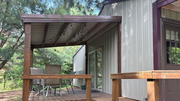 A wooden deck with chairs and a table, a covered porch, and a building with a window. - Shawnee Pines #2 - Studio (Golconda)