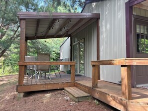 A wooden deck with chairs and a table, a covered porch, and a building with a window.