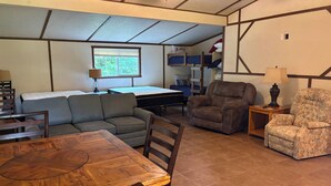 A room with a wooden dining table, a sofa, a recliner, a bunk bed, and a window with blinds. - Shawnee Pines #2 - Studio (Golconda)