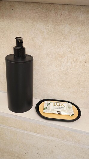 Ein schwarzer, zylinderförmiger Gegenstand und eine Schale mit einem Paket mit dem Aufdruck 'LUX BOTANICALS JAZMIN CREMOSO' auf einer beigen Fläche.